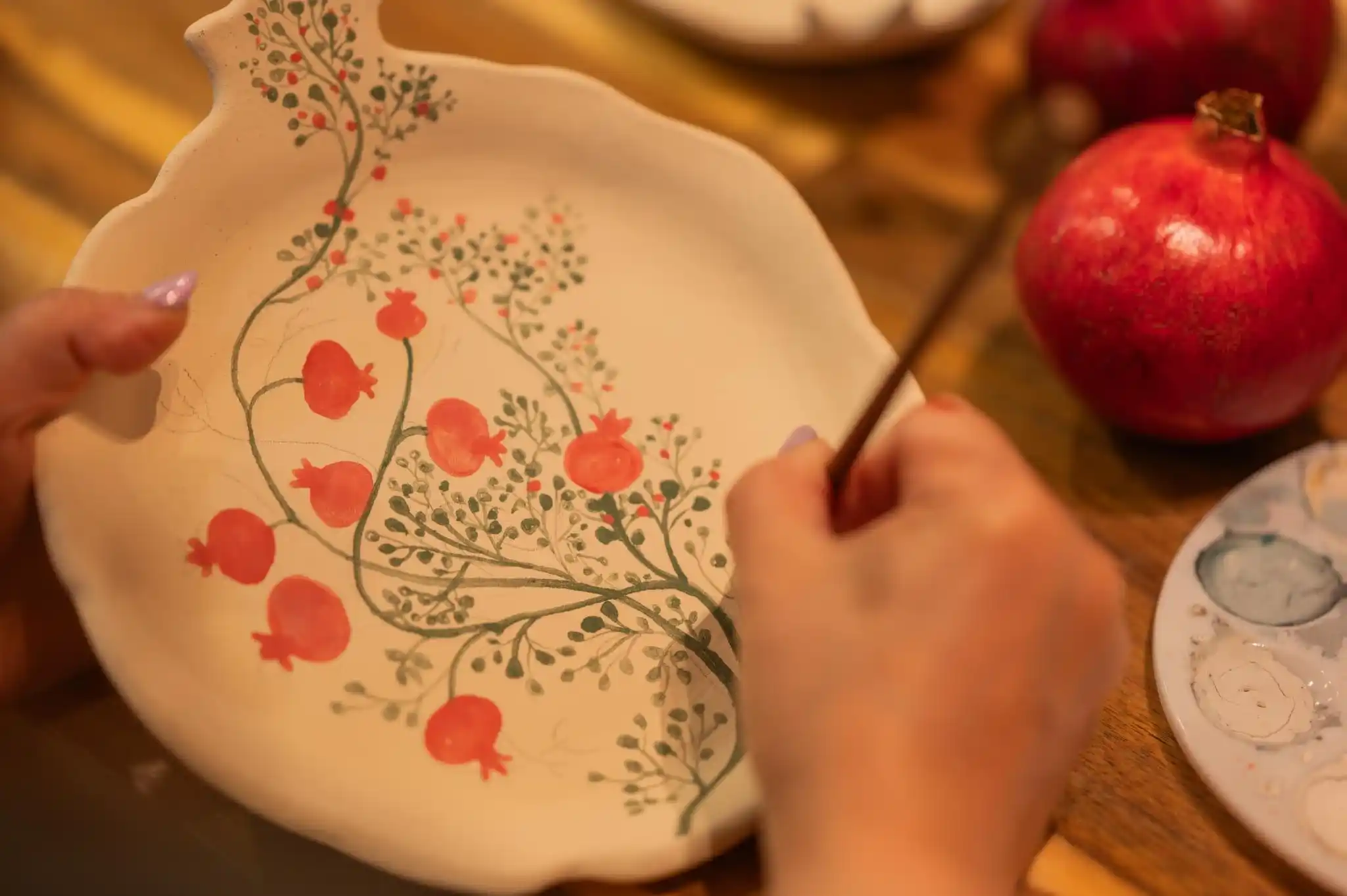 Hand-painting a pomegranate design on a ceramic plate