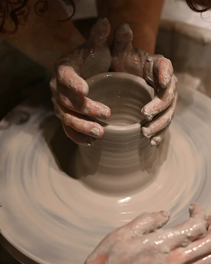 Clay-covered hands shaping a cylinder on the pottery wheel