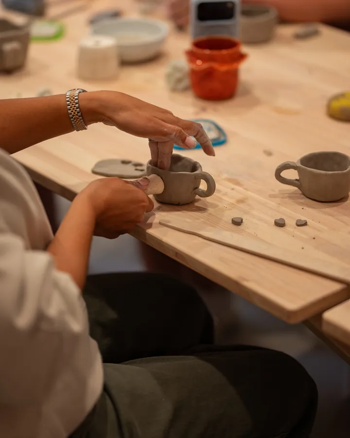 A student shaping a small cup at the hand building table