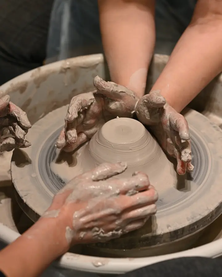 An instructor's hands and a student's hands centring clay together