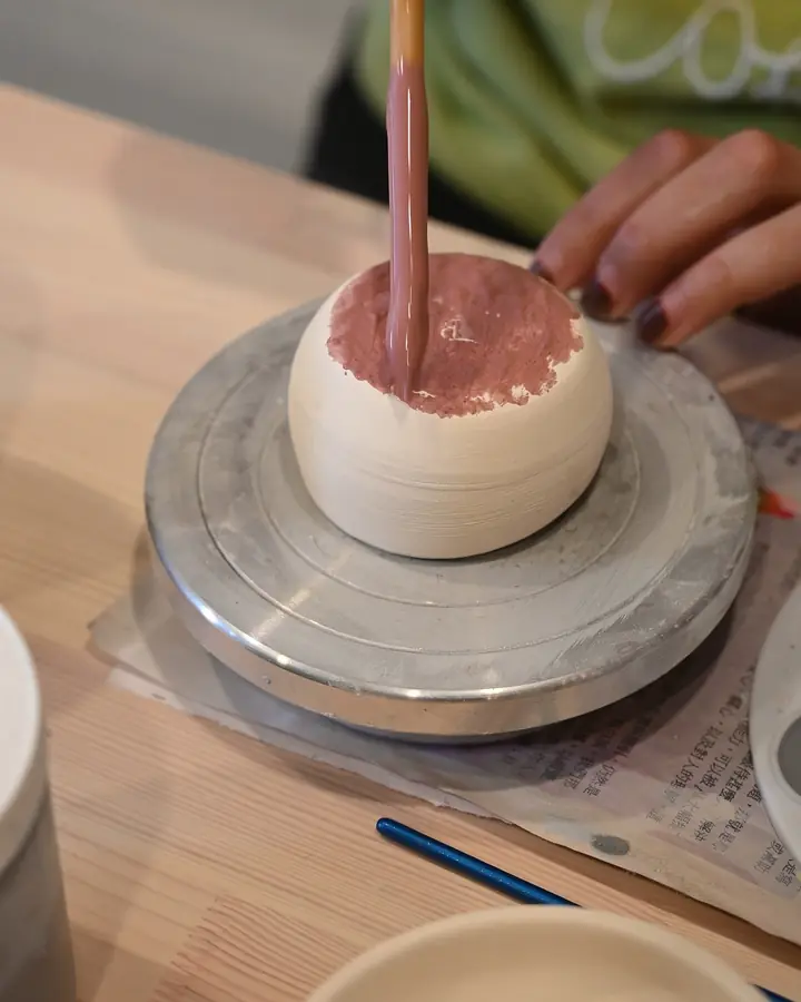 Pink glaze being brushed onto a bisque bowl