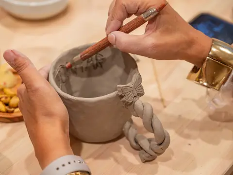 Hands carving a name into a cup with a braided handle