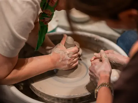 An instructor and a student centring clay side by side