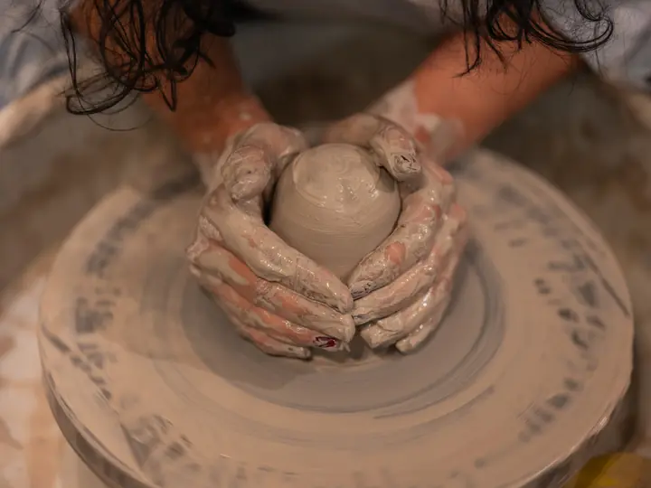 A beginner's clay-covered hands centring clay on the wheel