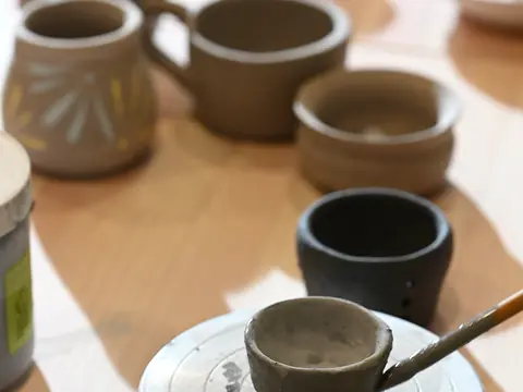 Glazing a small cup with finished mugs all around
