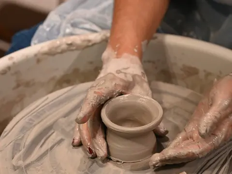 A finished pot being cut off the wheel with a wire