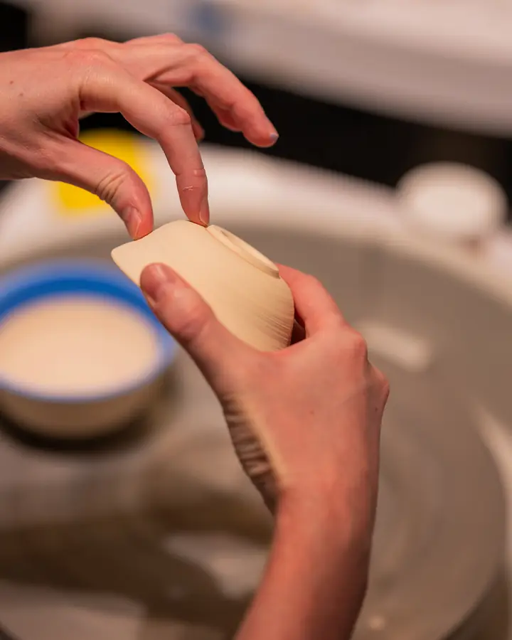 A student lifting a freshly thrown bowl off the wheel
