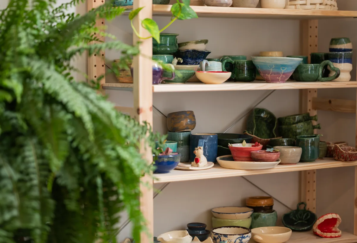 Glazed bowls and cups on the pickup shelves beside a fern