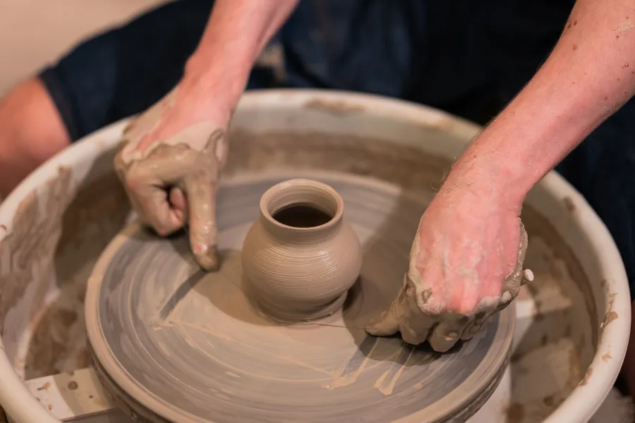 Clay-covered hands shaping a small pot on the pottery wheel