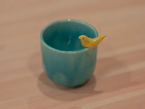 A turquoise cup with a little yellow bird on the rim
