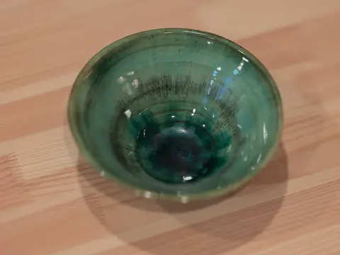 A green glazed bowl with a dark pool of glaze in the centre