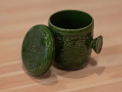 A textured green jar with its lid beside it