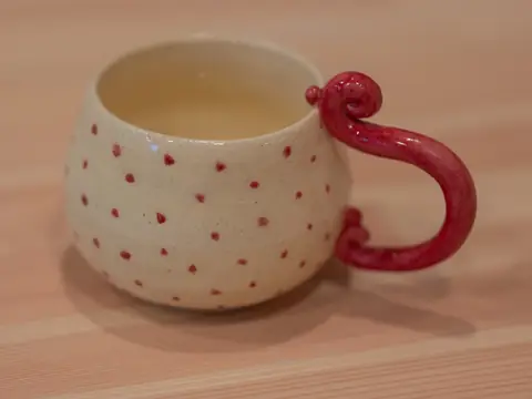 A white mug with red polka dots and a curled red handle