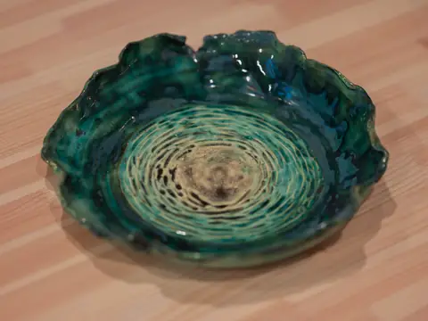 A wide green bowl with a wavy rim and carved rings