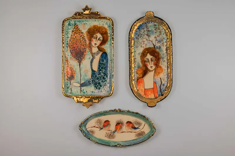 A curated collection of three ceramic artworks displayed together, showcasing portrait work and bird motifs.