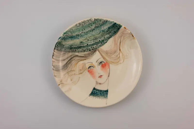 A beautiful ceramic plate showcasing a female portrait with flowing blonde hair and intricate patterned clothing.