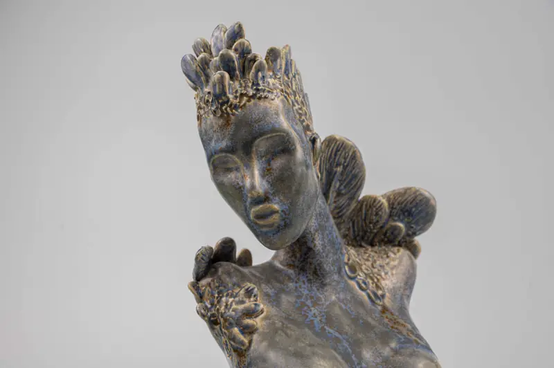 A serene sculptural ceramic piece featuring a meditative face with closed eyes and intricate decorative elements.