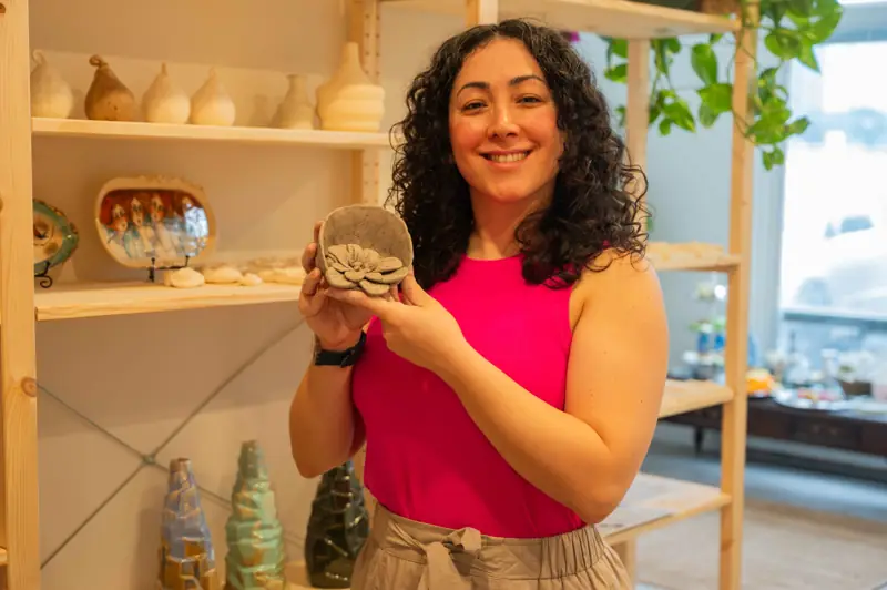 A student smiling and holding up the bowl she made
